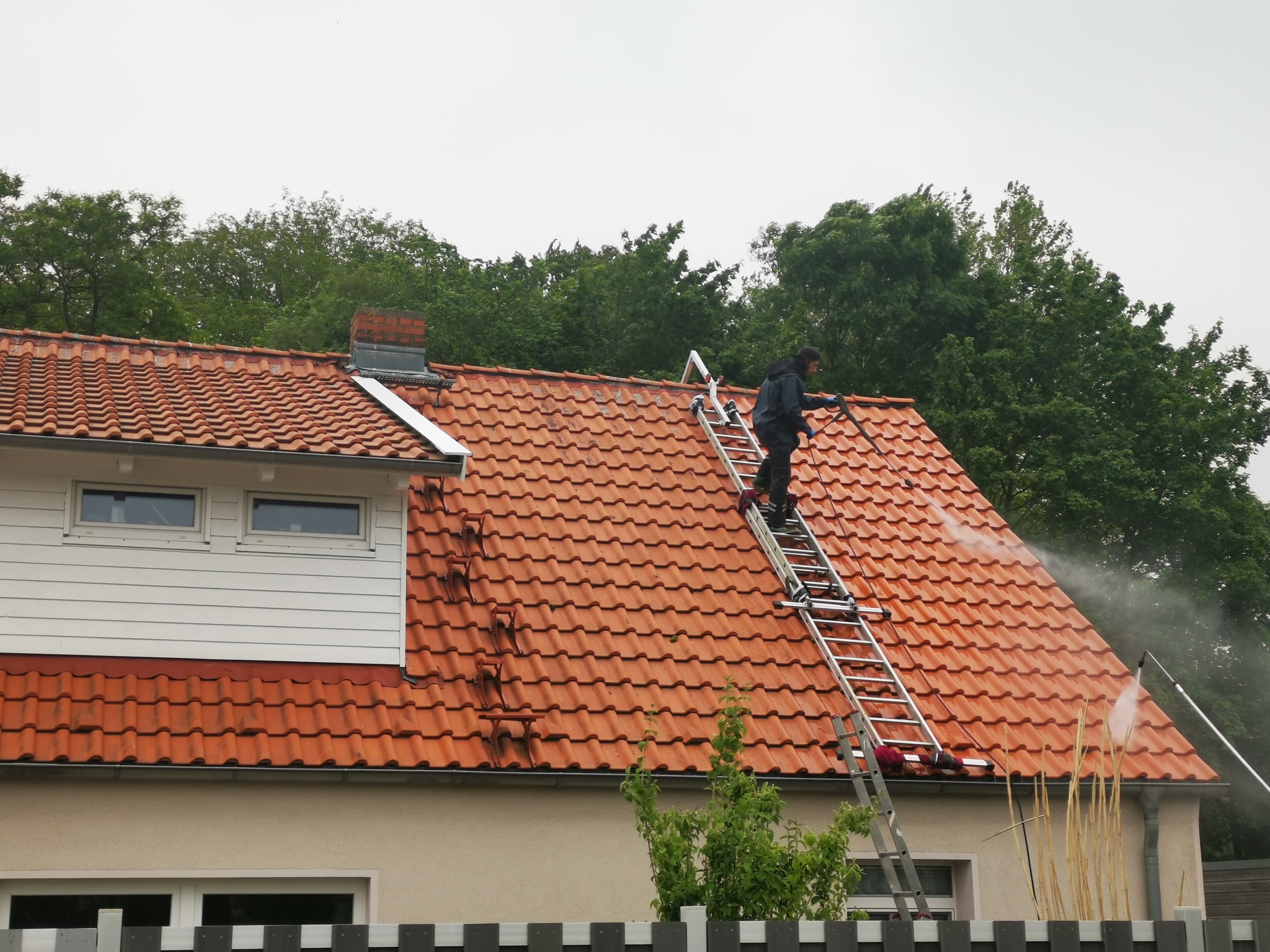 Zwei Mitarbeiter reinigen das Dach eines Wohnhauses
